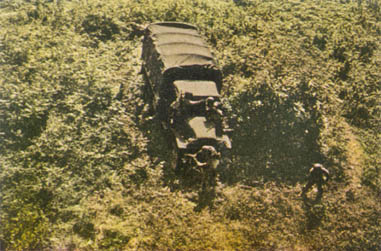 [FIGURE 49 (a). Steps in the erection of a drape.  In upper picture, truck is parked close to bush.  Reflecting surfaces which may shine are covered before the net is put on.  Rear curtain is dropped to cover shadow in cargo space.]